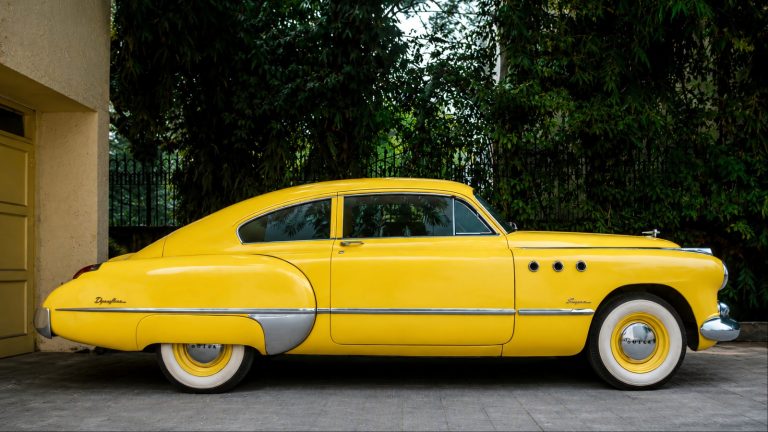 A vintage yellow car is standing in an auction showcase