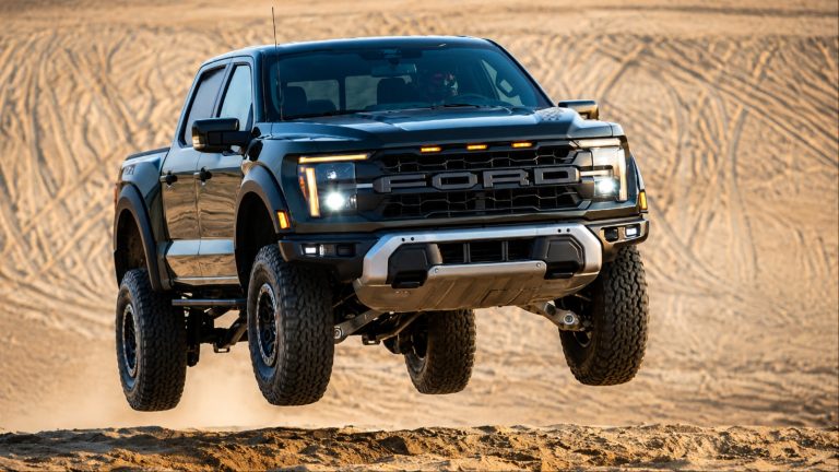 A Ford F-150 Raptor launches over sandy terrain with all four wheels airborne