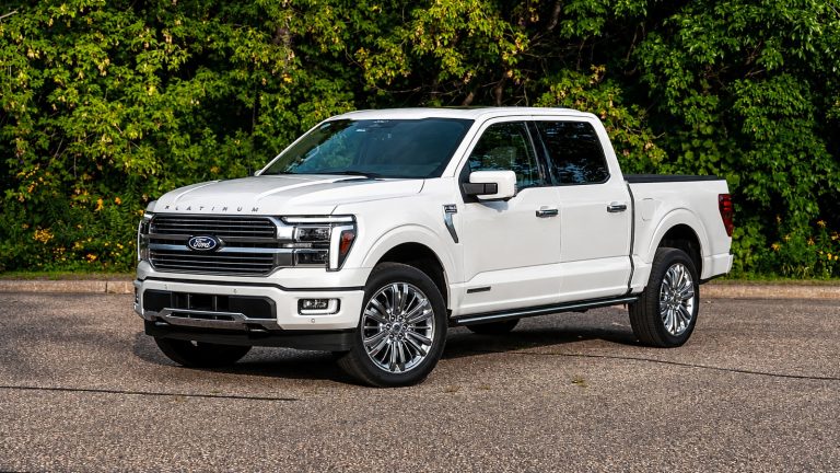A white Ford F 150 Hybrid is standing in front of small plants