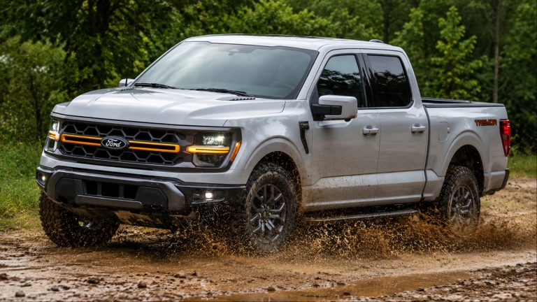 Ford F-150 Tremor powers through muddy terrain, splashing water along a wooded trail