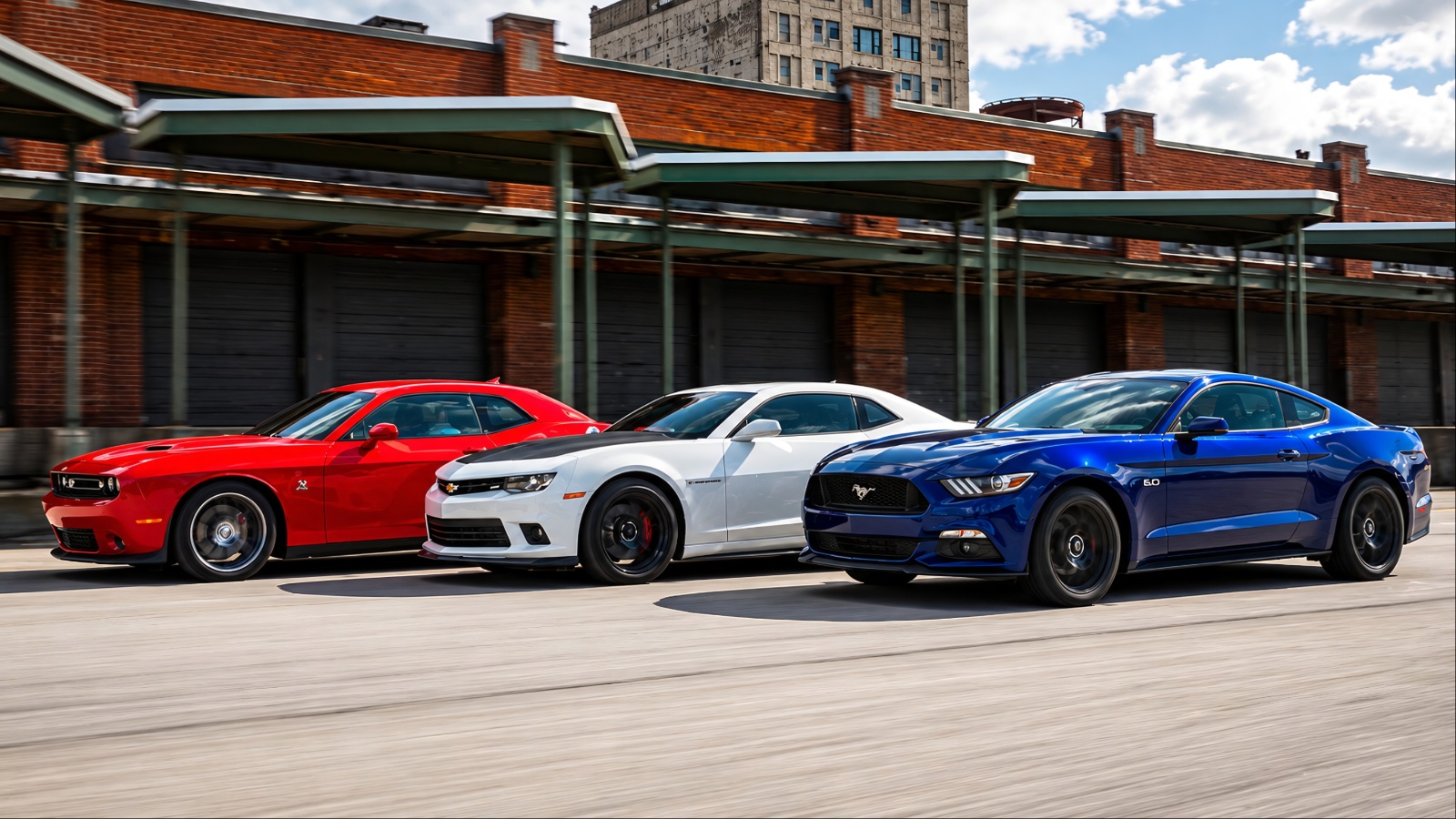 Ford Mustang, Chevrolet Camaro, and Dodge Challenger cruise side-by-side downtown