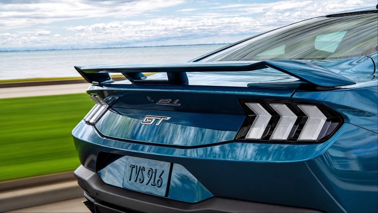 Rear view of a teal Ford Mustang GT driving along a coastal road with motion blur