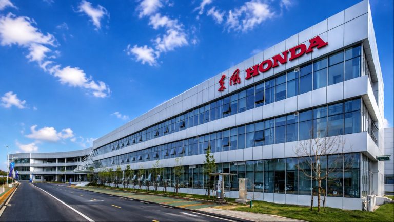 Honda facility with a modern glass exterior, roadway, and landscaped grounds