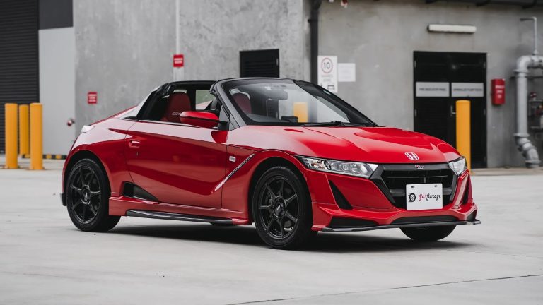 Honda S660 sports car parked outside an industrial facility, showcasing its compact convertible design