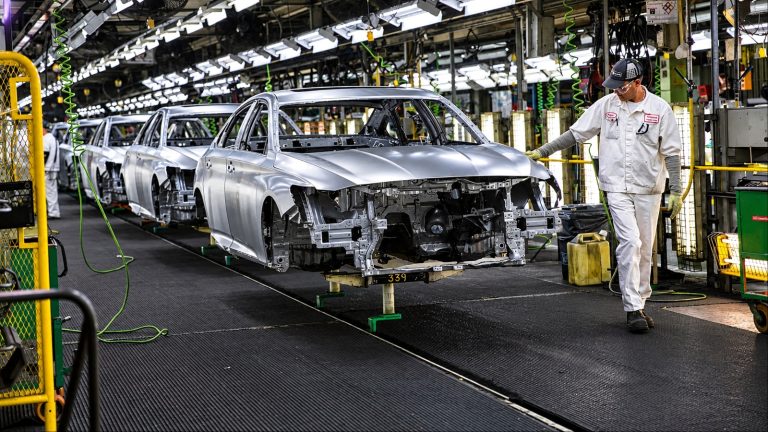 Worker in white uniform inspecting car bodies on an assembly line