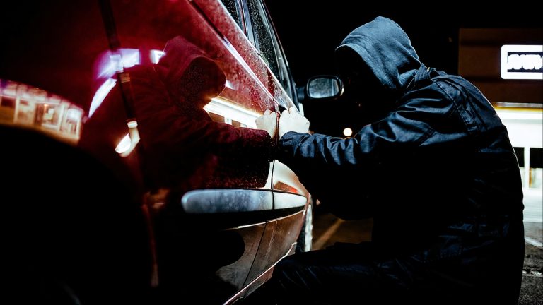 hooded figure quietly attempts to break into a vehicle
