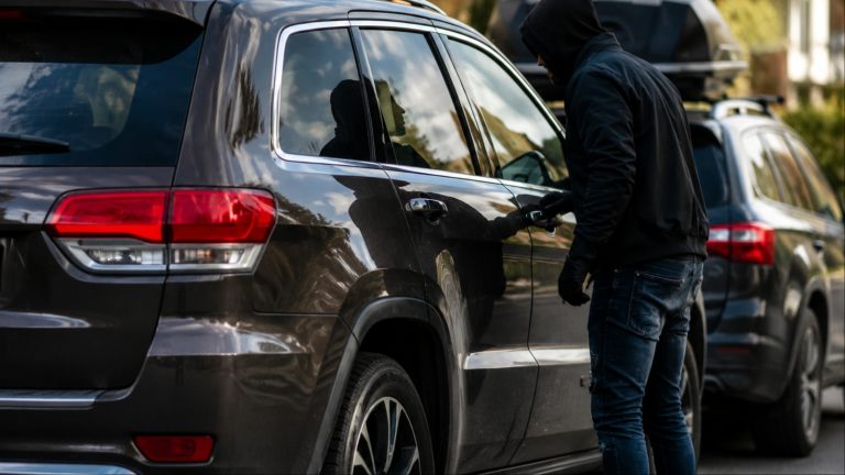 hooded individual attempting to open the door of a dark suv