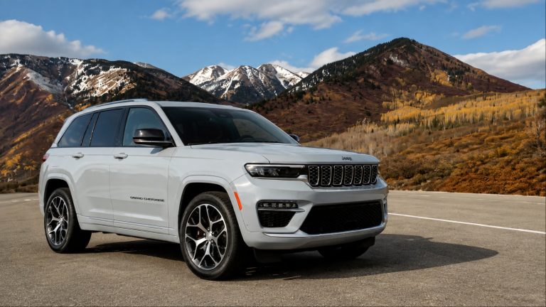 Jeep Grand Cherokee parked on a mountain road, with snow-capped peaks and rugged terrain in the background