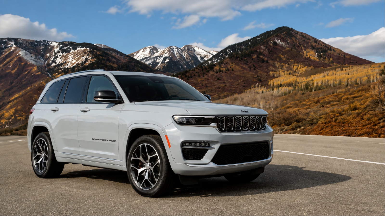 Jeep Grand Cherokee parked on a mountain road, with snow-capped peaks and rugged terrain in the background