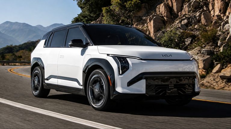 white and black Kia SUV driving along a scenic winding mountain road under a clear sky