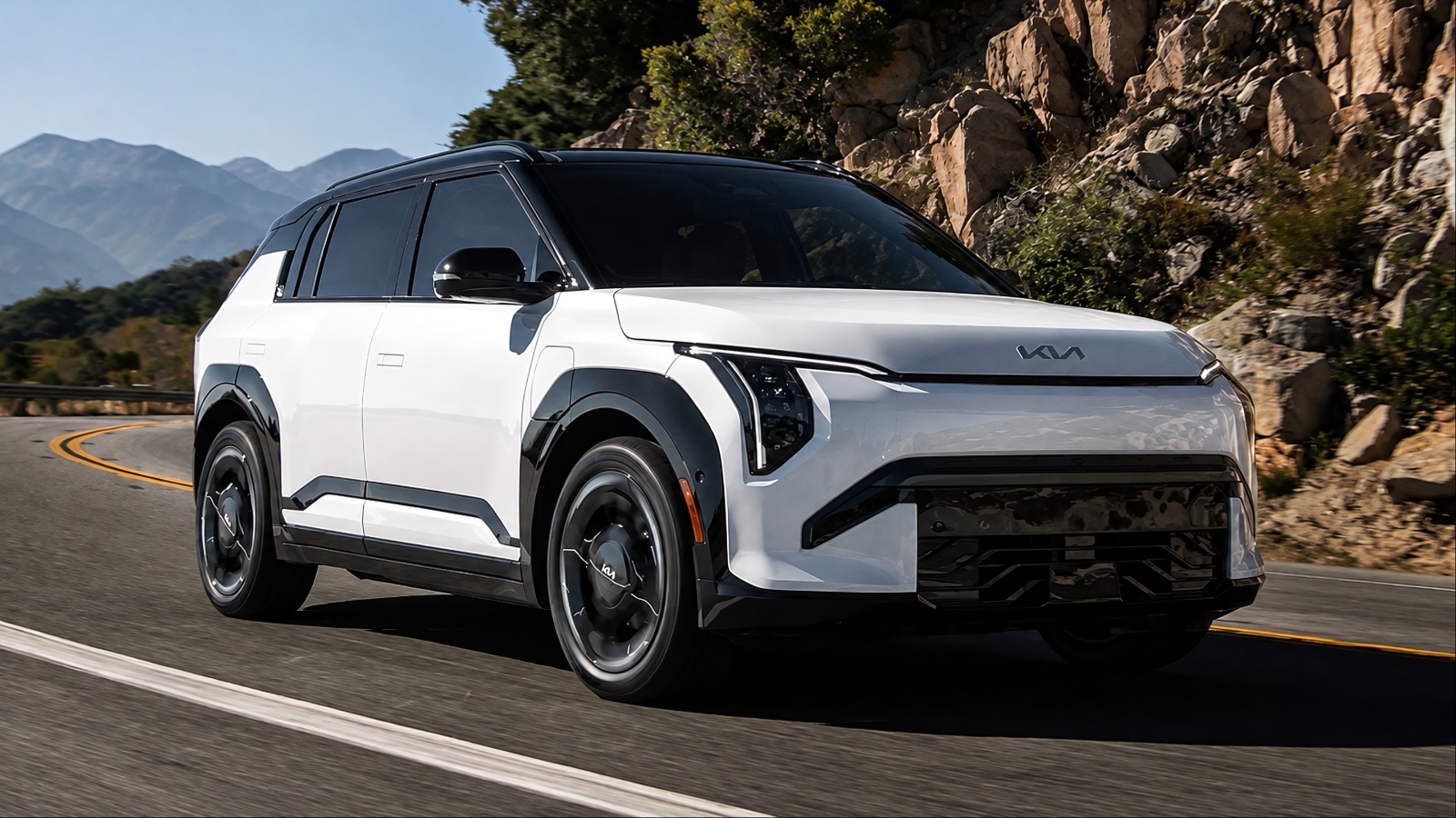 white and black Kia SUV driving along a scenic winding mountain road under a clear sky