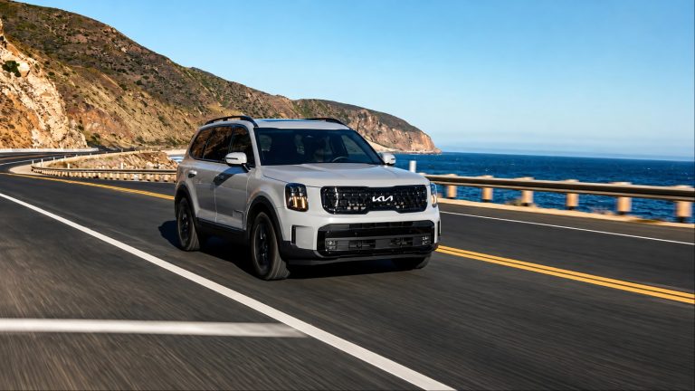 Kia Telluride drives along a scenic coastal highway with mountains and ocean