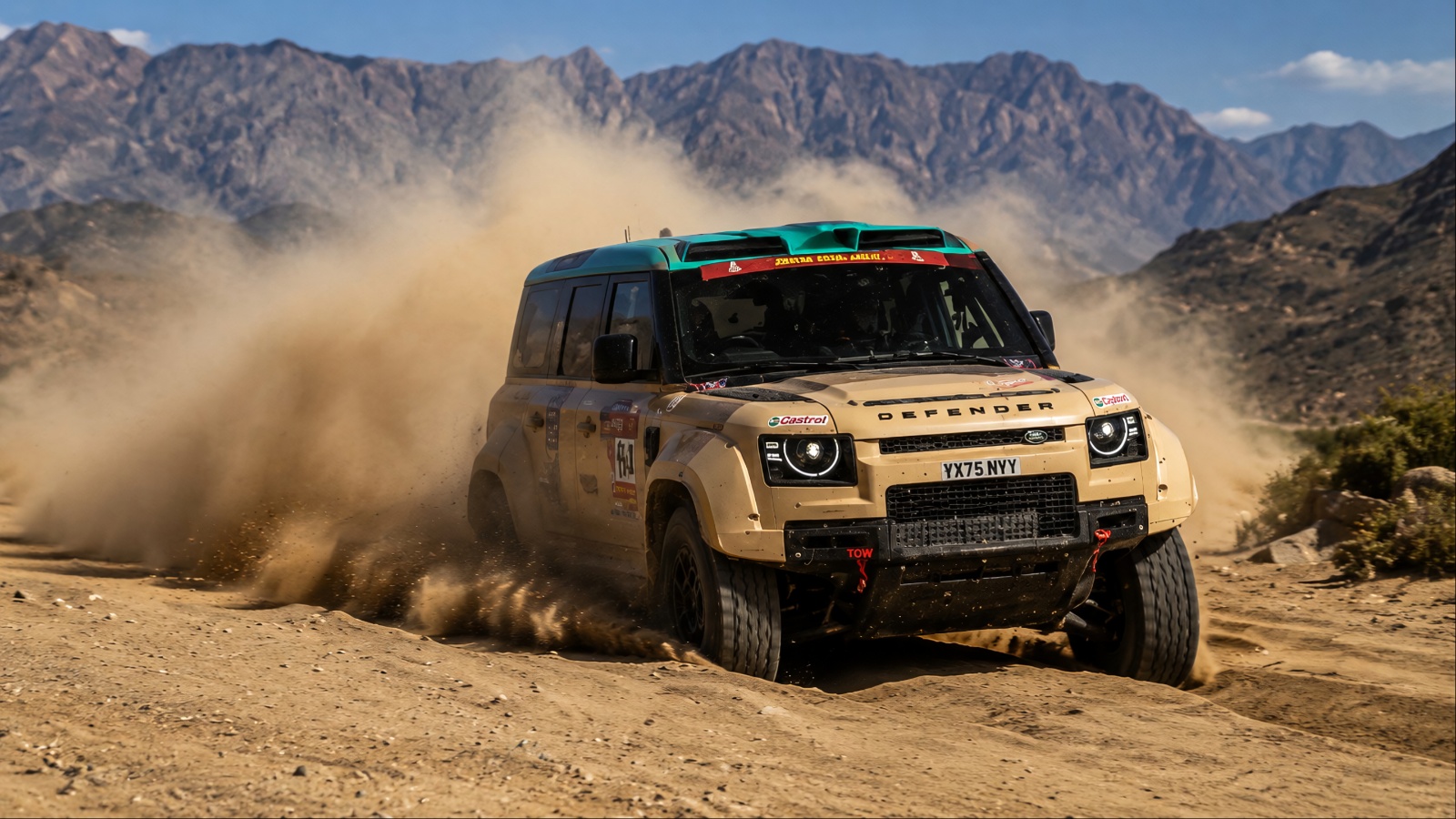 Land Rover Defender racing through desert terrain, kicking up dust against rugged mountains