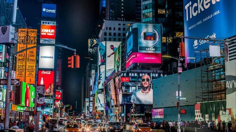 Bright neon billboards illuminate a crowded New York City street at night with glowing advertisements
