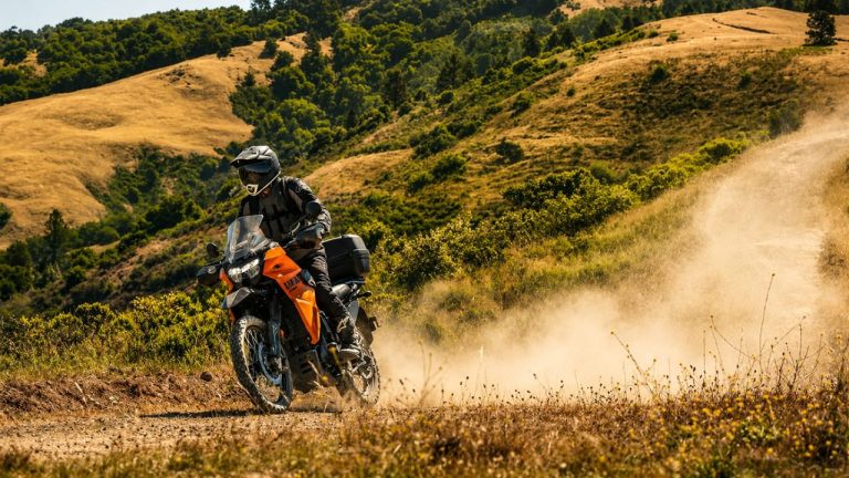 Off-road adventure motorcycle speeding along a dusty trail through scenic golden hills