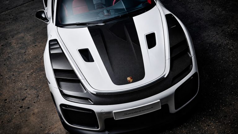 High-angle view of white Porsche sports car front hood featuring exposed carbon fiber vents and details
