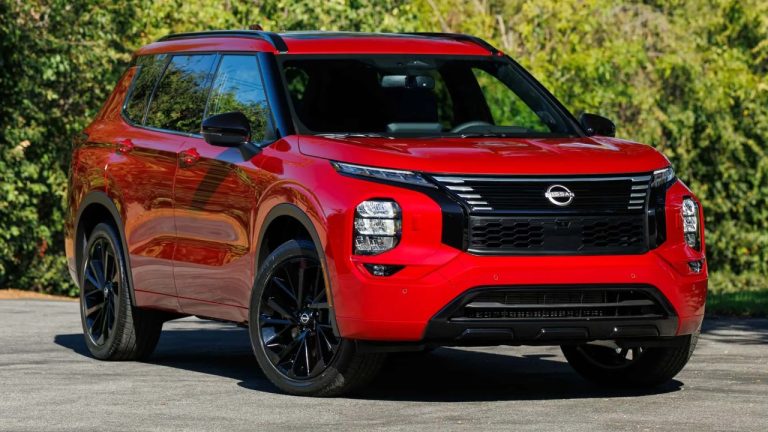 Red Nissan Rogue parked outdoors against a lush green background