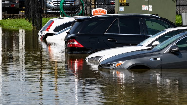 Several vehicles sit partially submerged in floodwater at a flooded parking area
