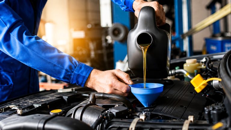 Mechanic pours motor oil into car engine via blue funnel