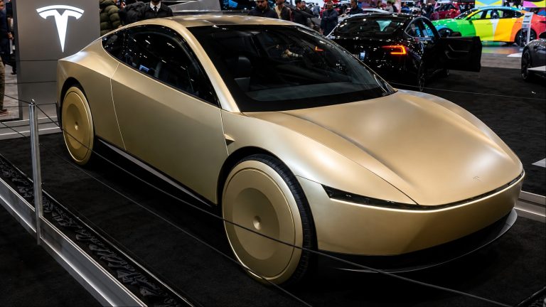 Tesla Cybercab displayed at an auto show, surrounded by other vehicles and attendees