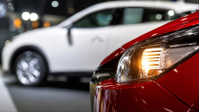 Red car headlight closeup with white car blurred in background