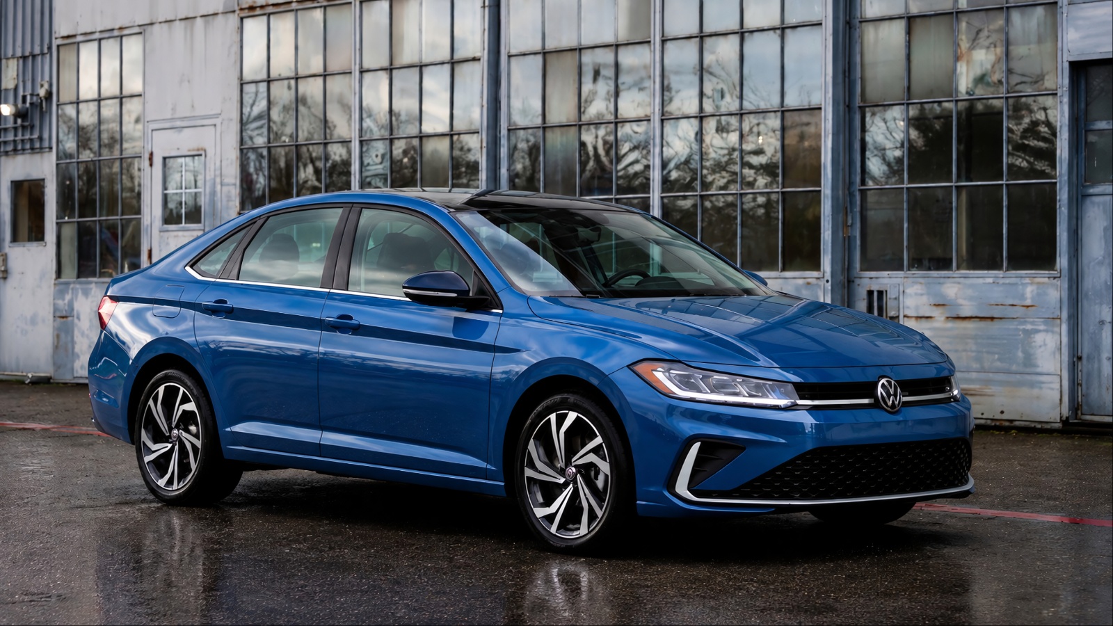 A blue Volkswagen Jetta parked outside an industrial-style building with large windows