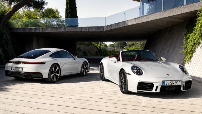 White Porsche 911 Carrera S coupe and convertible parked beneath a modern concrete structure