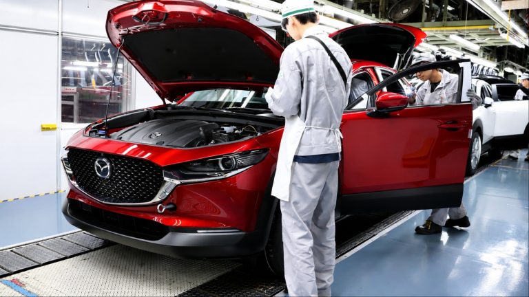Workers inspect a Mazda vehicle during production inside a modern automotive factory