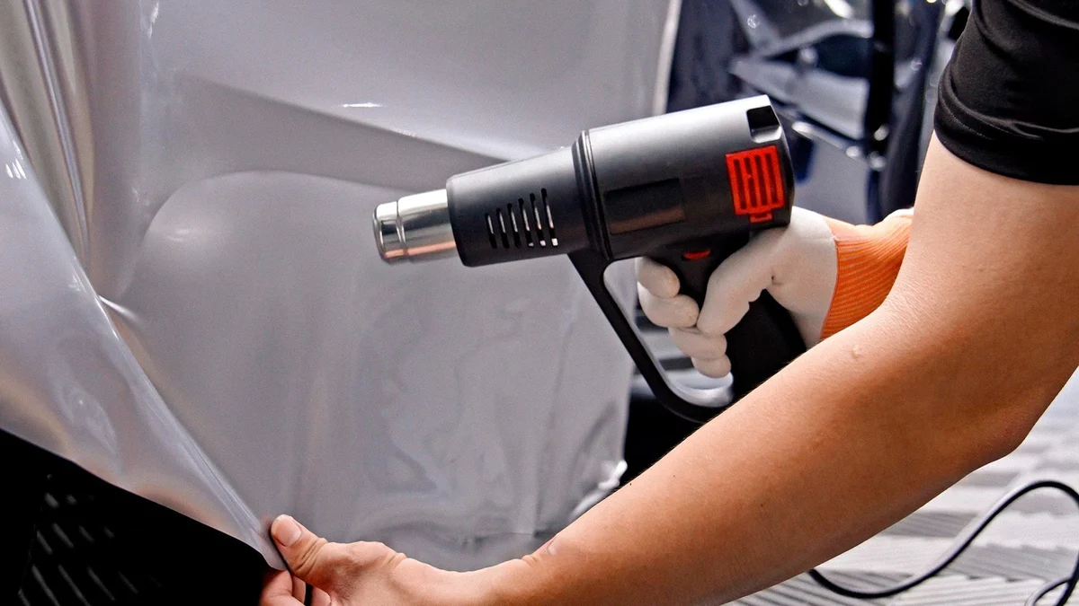 A man is trying to wrap a car with the help of a heat gun