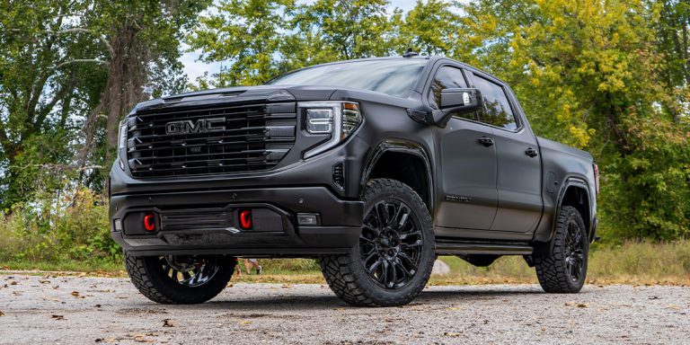 A GMC Sierra is standing in front of green trees