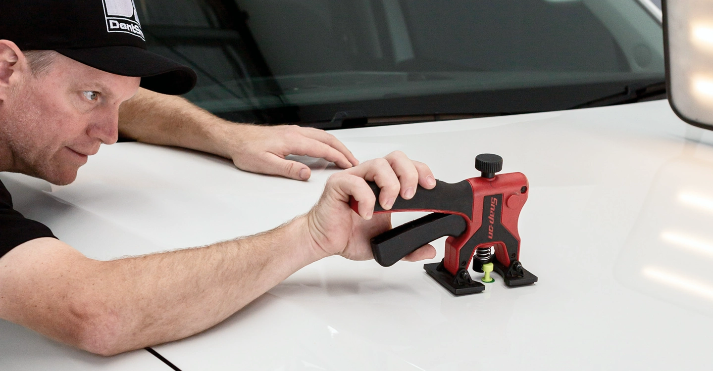 A mechanic is trying to remove the dent with a tool