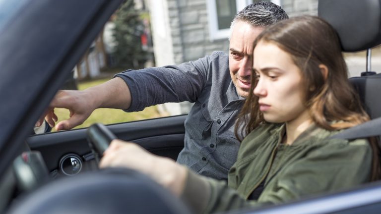 A father is trying to guide her teenage child on how to drive
