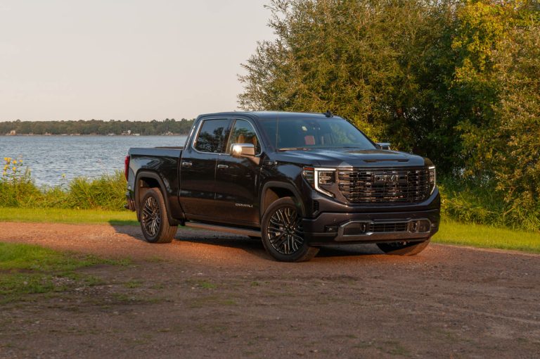 A black Sierra Denali is standing on a rough patch of road near a water body