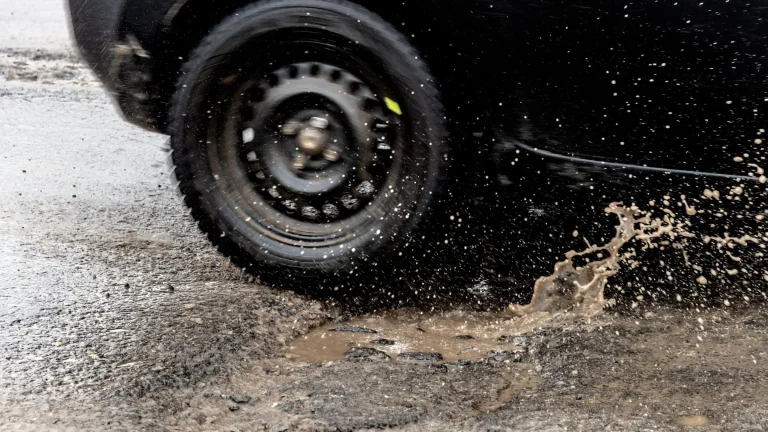 A car is driving at high speeds through a muddy pothole