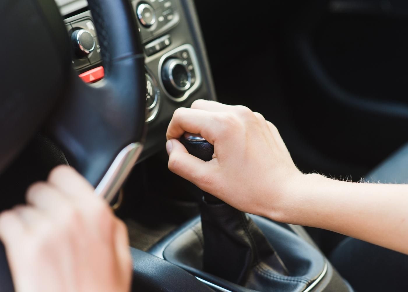 Driver shifting a manual transmission in a modern car interior while driving