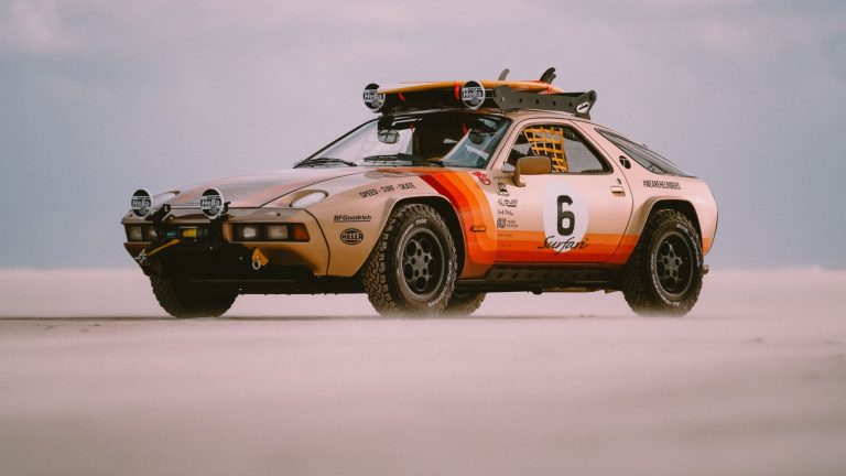 A Porsche in a modified state is cruising on a sandy road