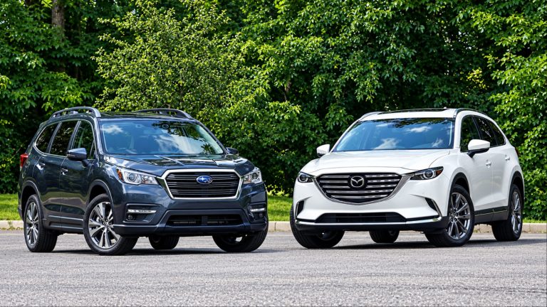 Two SUVs a dark Subaru and white Mazda parked by green trees