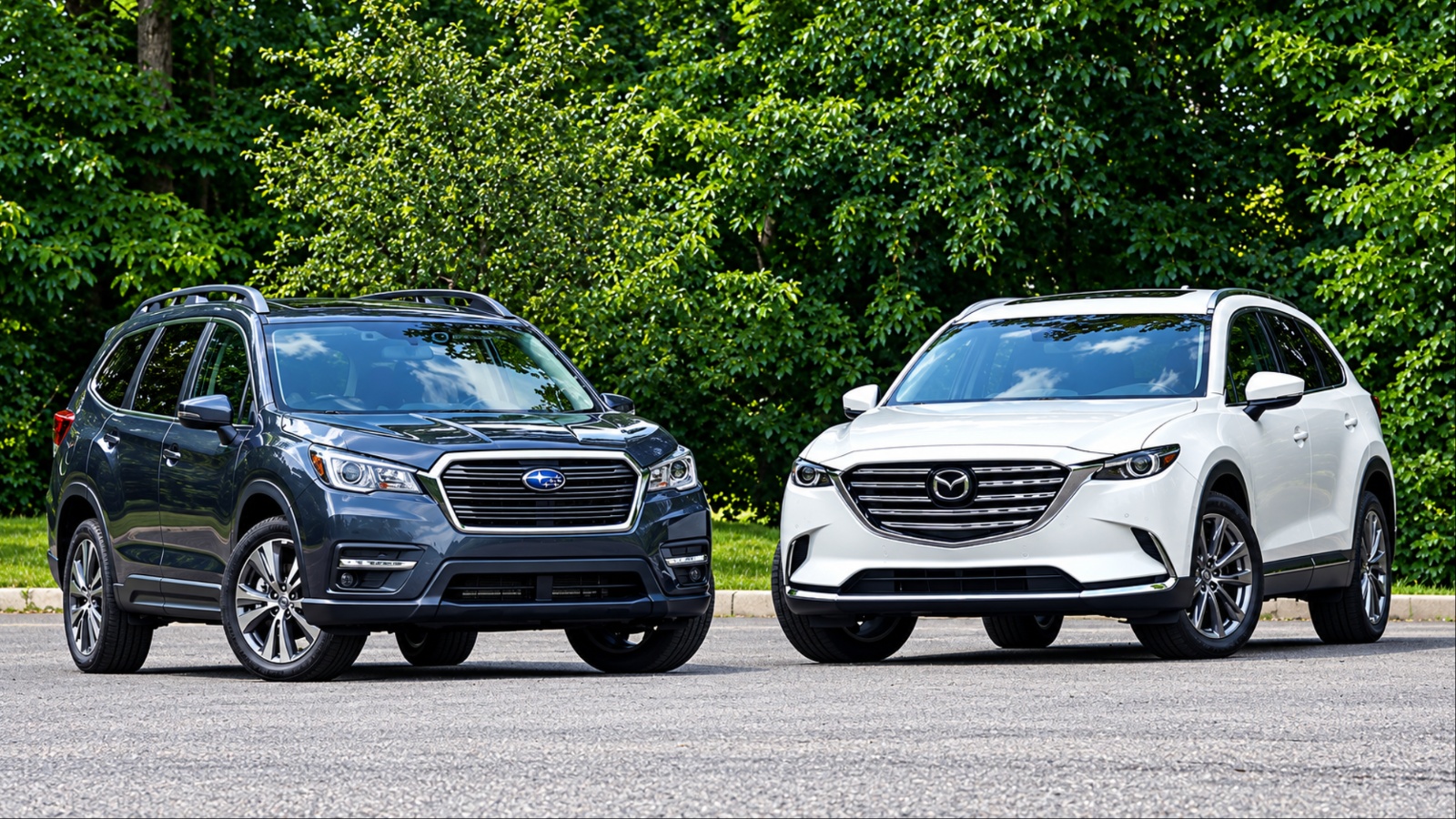 Two SUVs a dark Subaru and white Mazda parked by green trees