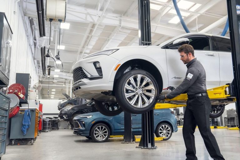 Dealer technician inspecting a vehicle on a service lift during manufacturer warranty repair work