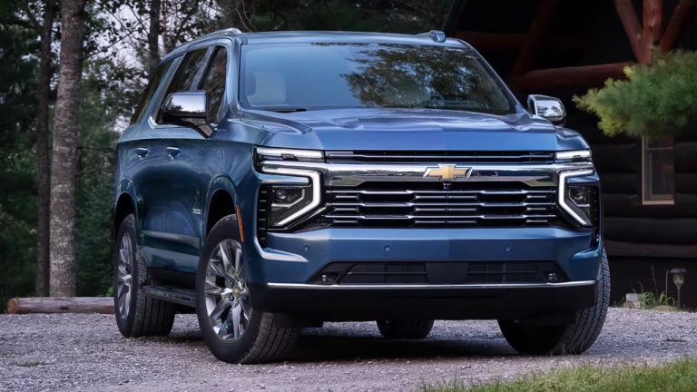 A blue Chevrolet Tahoe parked outdoors near a rustic cabin surrounded by trees
