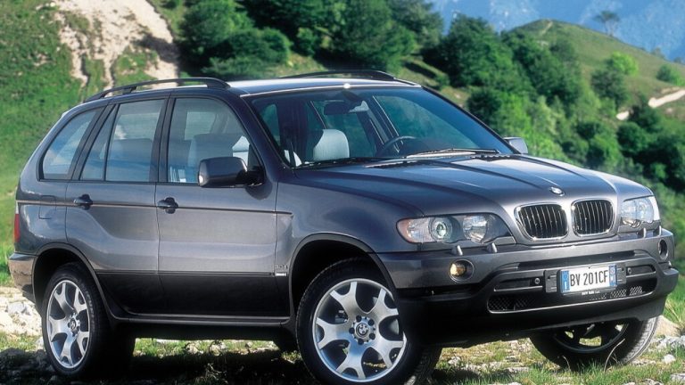 A first-generation BMW X5 is pictured against a scenic mountainous landscape
