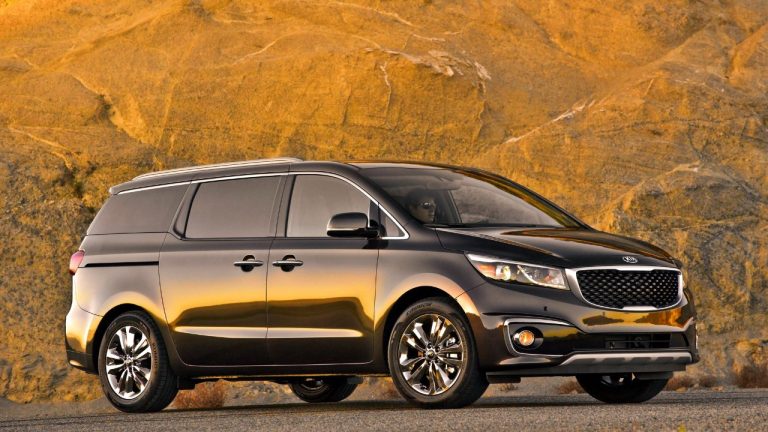 A Kia Sedona minivan sits against a rugged rock backdrop at sunset