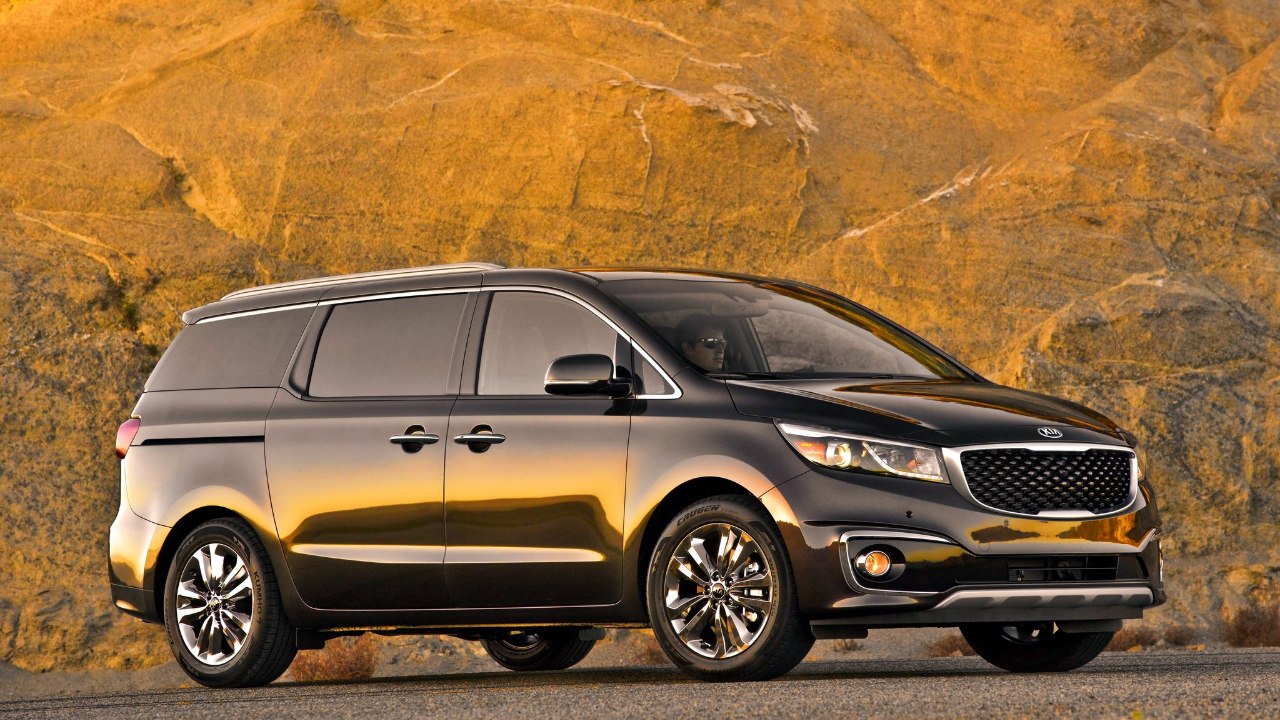A Kia Sedona minivan sits against a rugged rock backdrop at sunset