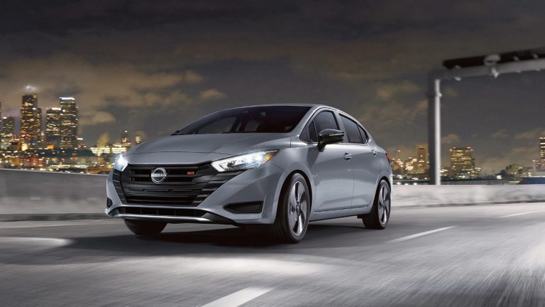A Nissan Versa drives through the city at night under bright lights