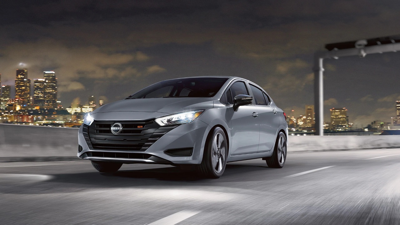 A Nissan Versa drives through the city at night under bright lights