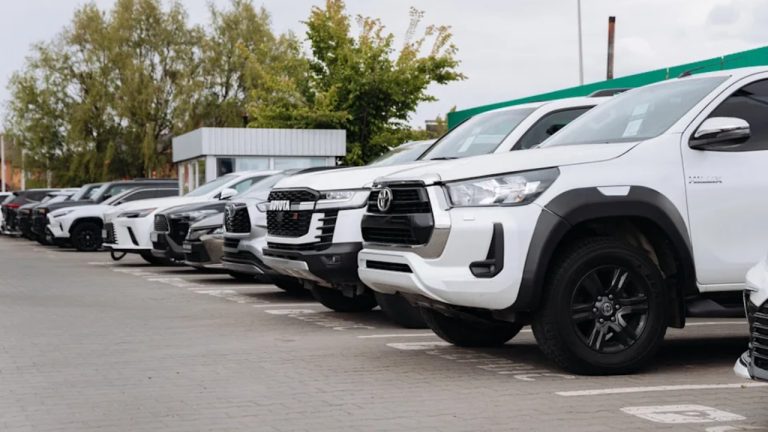 A row of new pickup trucks and SUVs sits outside a dealership