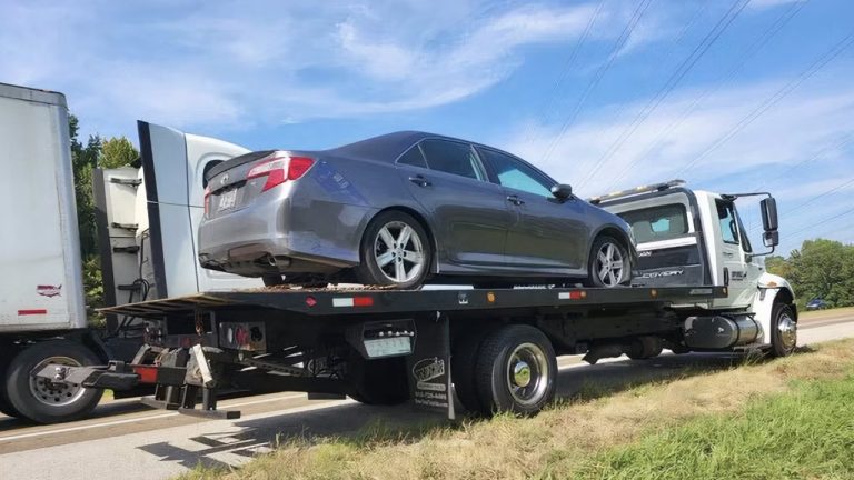 A sedan is secured on a flatbed tow truck beside the roadway
