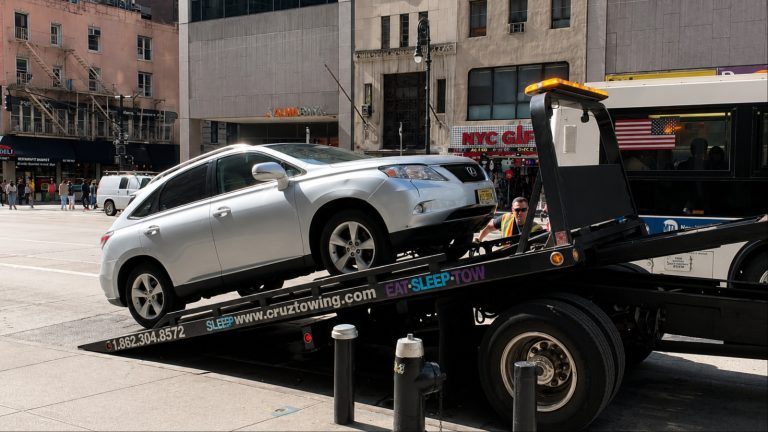 A silver SUV being towed through a busy New York City street