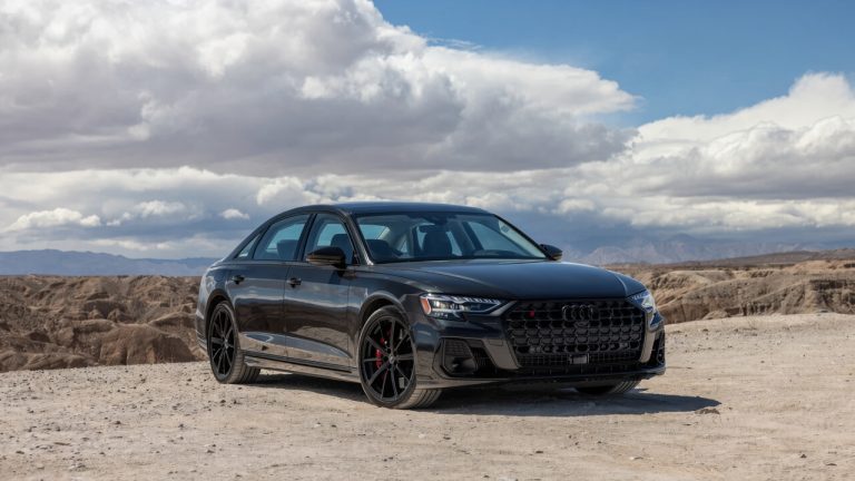 Audi S8 parked against a dramatic desert landscape beneath a cloudy blue sky