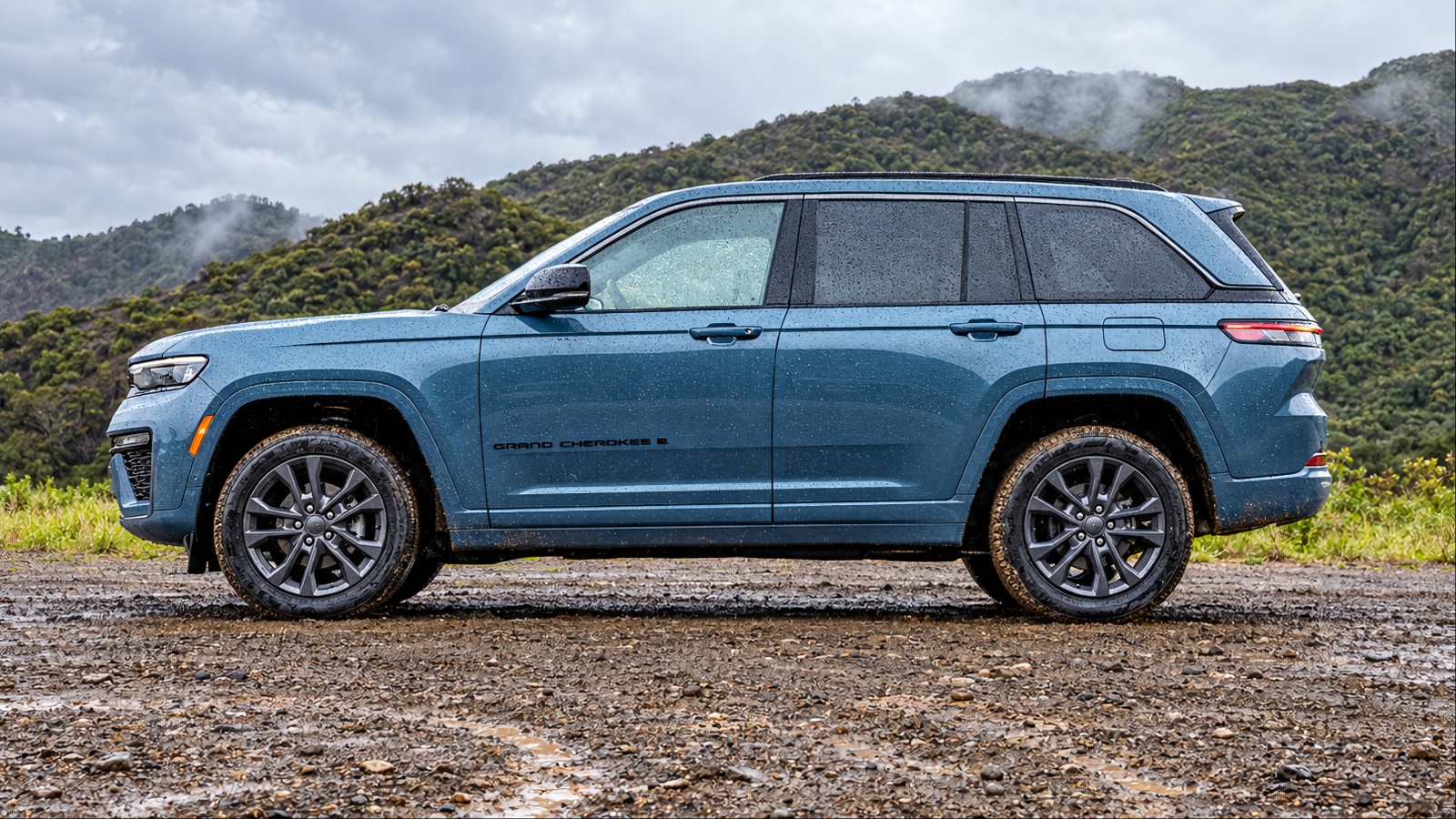 A Blue Jeep Grand Cherokee is standing on a muddy road